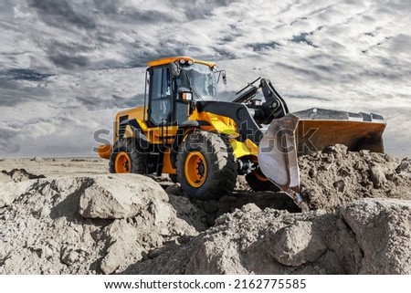 Bulldozer or loader moves the earth at the construction site against the sunset sky. Contrasting image of a modern loader or bulldozer. Construction heavy equipment for earthworks