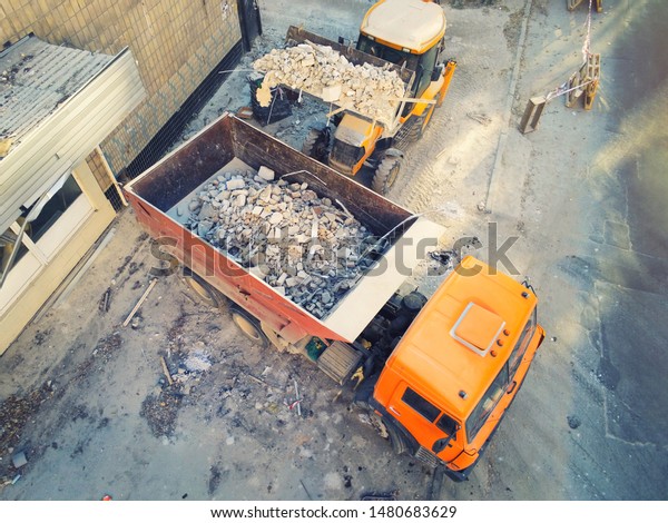 Bulldozer loader\
uploading waste and debris into dump truck at construction site.\
building dismantling and construction waste disposal service.\
Aerial drone industrial\
background