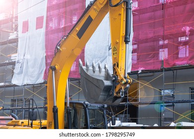 Bulldozer Near The Construction Site And Facade Covered With Green Protective Polypropylene Mesh And With Scaffolding, Buldozer Blade Closeup View