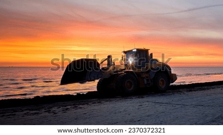 Bulldozer on the beach at sunset. A large tractor cleans the beach of sea grass. Bulldozer in motion and blur.