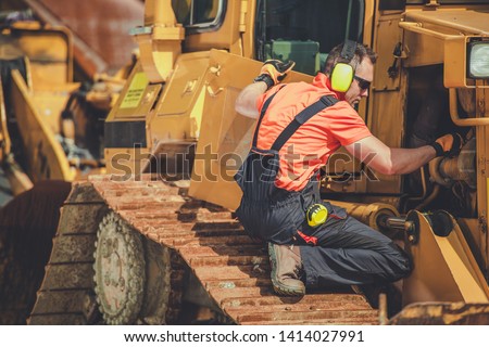 Bulldozer Professional Mechanic. Caucasian Technician Taking Machine Under Maintenance. Construction Heavy Duty Equipment.