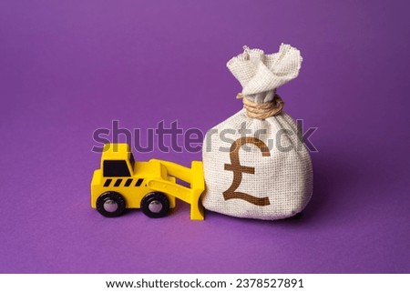 A bulldozer pushes a british pound sterling moneфy bag. Ineffective use of funds. Money down the drain. Financing of dismantling works. Demolition services, land leveling. Industry machinery for rent.