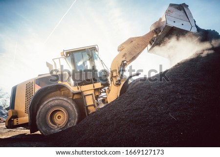 Bulldozer putting biomass on pile for composting in industrial facility