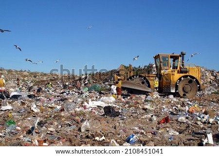 A bulldozer working at a landfill site, with laborers picking waste for recycling.