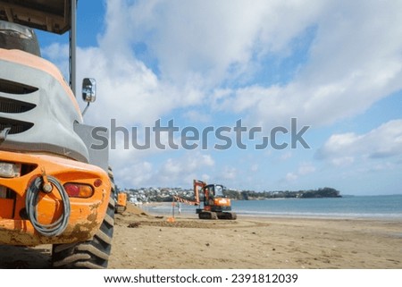 Bulldozers working on Milford beach, selective focus on one bulldozer in the foreground. Auckland.
