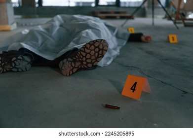 Bullet shell as clue. Dead body of a man is on the ground, covered in white cloth. Conception of murder, homicide.
