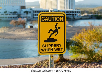 Bullhead, AZ / USA – February 19, 2020: Caution Slippery When Wet sign at the water taxi dock in Bullhead City, AZ, with a background of the Riverside Hotel and Casin in Laughlin, NV and the Colorado 