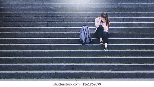 Bullying, discrimination or stress concept. Sad teenager crying in school yard. Upset young female student having anxiety. Upset victim of abuse or harassment sitting on stairs outdoors with backbag. - Powered by Shutterstock