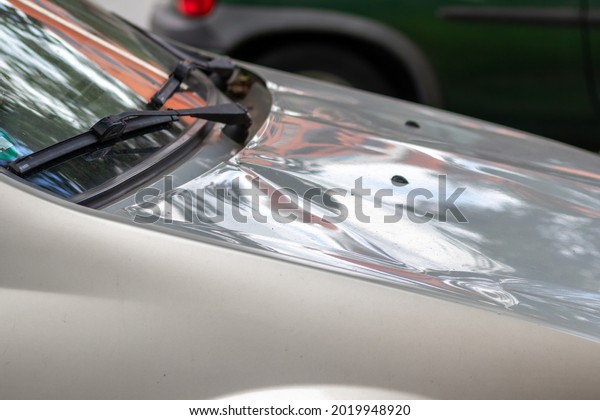 Bumped car engine hood after heavy storm as\
extreme weather and fallen trees and hail damage shows car\
insurance needs for auto repair and weather insurance for victims\
and emergency coverage\
danger