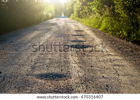 Bumpy dirt road with holes against sunshine in background. Shallow field of depth.