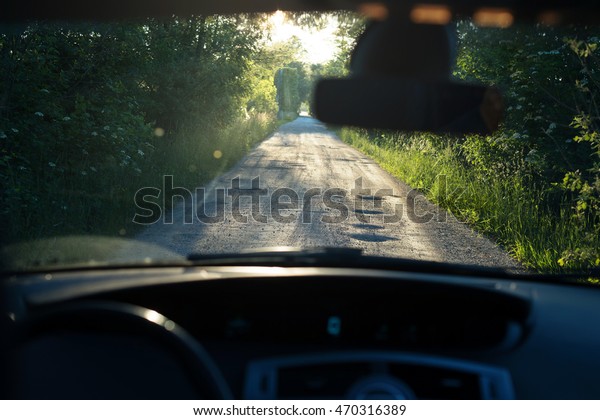 Bumpy dirt road with\
holes against sunshine in background shot through a windshield.\
Shallow field of depth.