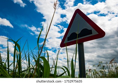Bumpy road ahead sign in tall grass and bright clouds and blue sky in background