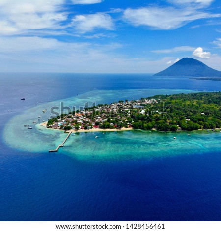 Bunaken Island from above surrounded by a coral reef with mountain in the background