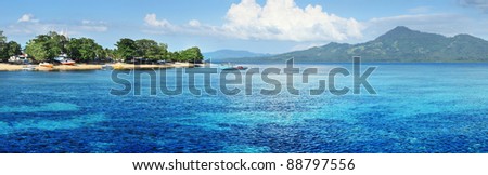 Bunaken island (left) with boats and wooden buildings in trees. North Sulawesi. Indonesia