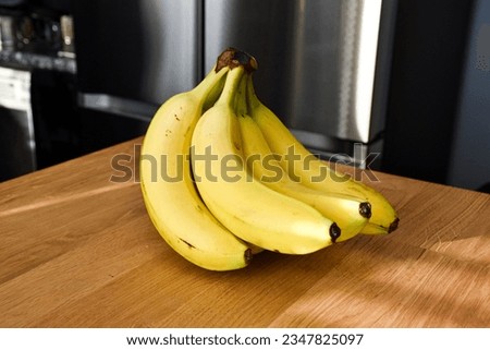 A bunch of bananas lying on a solid wooden table. Sweet ripe bananas with yellow skin