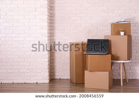 Bunch of blank unsigned moving boxes with blank screen laptop on top in new empty apartment. Spacious unfurnished room with unpacked cardboard box stack. Interior background, copy space for text.