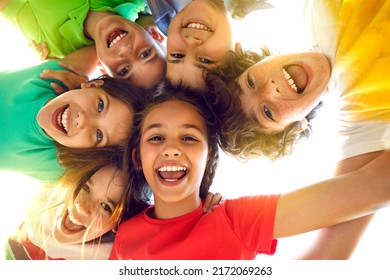 Montón de alegres y adorables niños pequeños jugando juntos y divirtiéndose. Retrato grupal de niños felices acurrucándose, mirando hacia abajo a la cámara y sonriendo. Ángulo bajo, vista desde abajo. Concepto de amistad