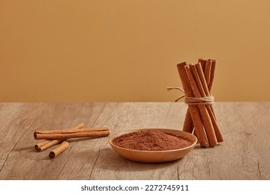 A bunch of cinnamon sticks standing next to a wooden dish of cinnamon powder on a wooden table. cinnamon (Cinnamomum) is useful for cooking and also good for health
