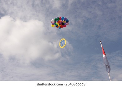 A bunch of colorful balloons floats up into a cloudy sky. Below them is a yellow circle with a blue pi symbol. A red and white flag hangs from a pole on the right side of the frame.
