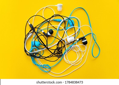 Bunch of different earphones isolated on yellow background. Color conceptual. Conceptual minimalism. Minimal thing. Minimal think. Tangling bunch of earphones wires. Tangled cable