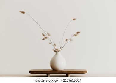 A bunch of  dried bunnytail flower in a white ceramic vase on a brown wooden board. Simple and minimal home decoration. White wall, copy space. 