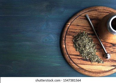    A bunch of dried leaves yerba mate tea with a bombilla stick and traditional calabash for drinking on wooden plate. Selective focus, top view, copy space for your text.