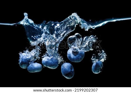 Bunch of fresh blueberries dropped in water with air bubbles and splashes isolated on black background.
