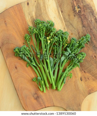 Bunch of fresh broccolini on rustic wooden cutting board in flat lay composition.