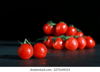 bunch of fresh cherry tomatoes with green stems isolated on dark grey marble table