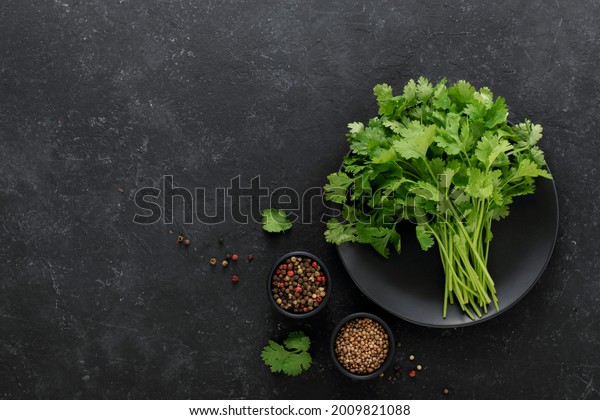 \
A bunch of fresh cilantro, salt,\
pepper on a black background, top view, copy\
space.