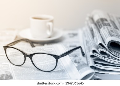 A bunch of fresh morning newspapers on the table in the office. The latest financial and business news in the daily newspaper. Cup of morning coffee, glasses. Information pages.

