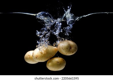 Bunch Of Fresh Potatoes Dropped In A Transparent Water Tank With Splashes On Black.