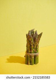 Bunch of fresh tied green asparagus heads standing on yellow background. Bright illumination with shadows.