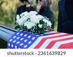 Bunch of fresh white roses and chrysanthemums on top of coffin covered with American flag during funeral service of passed away veteran