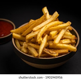 A Bunch of Fried Potatoes With Ketchup Behind All On Black Background
