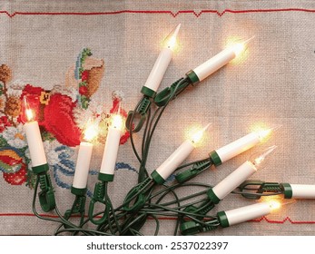 A bunch of glowing old christmas lights on a vintage table cloth with a cross stitch pattern.