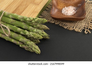 Bunch of green asparagus tied with jute cord near cutting board over a black background with copy space. Asparagus cooking and spring vegetable concept