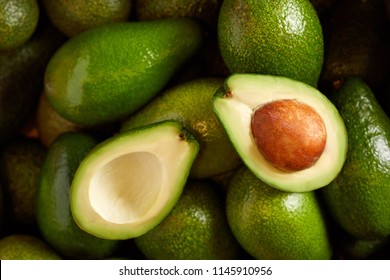 Bunch of green Avocados. One of them is opened that the stone and the pulp are visible