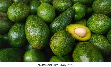 Bunch of green Avocados. One of them is opened that the stone and the pulp are visible.
