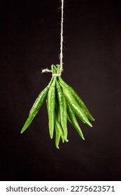 Bunch of green chili peppers hanging on a natural rope on a brown background - Shutterstock ID 2275623571
