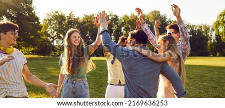 Bunch of happy young friends all together having fun on warm sunny day in summer park. Diverse group of cheerful joyful positive people standing on green lawn, smiling and giving each other high five