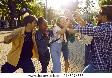 Bunch of happy young people give high five to their friend. Cheerful joyful diverse friends spending time together, enjoying good summer weather in the city, and having fun lots of fun