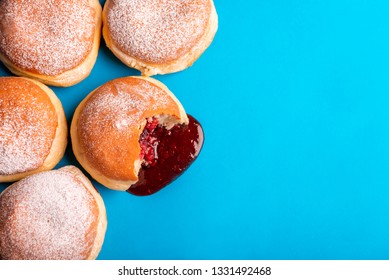 Bunch of jam doughnuts, filled with strawberry jelly, covered with powdered sugar, on a blue paper background. Flat lay with sweet food.