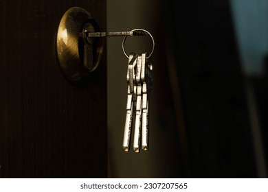 Bunch of keys sticks out of the door lock. Stainless steel keys protrude from a golden brass lock in a brown interior home door. Entrance door of the house with the keys in the copper lock. Close-up