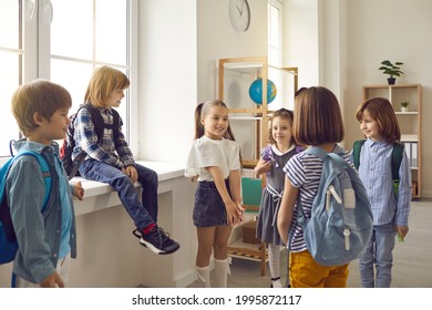 Bunch Of Kids With School Bags Standing In The Classroom And Talking. Group Of Cute Little Children Communicating With Each Other. Young School Boys And Girls Meet And Make Friends At School