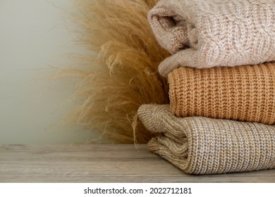 Bunch of knitted warm pastel color sweaters with different knitting patterns folded in stack, clearly visible texture. Stylish fall-winter season knitwear clothing. Close up, copy space for text.