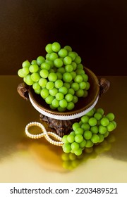 Bunch Of Korean Shine Muscat Grapes On Dark Gold Background. Retro Concept With Antique Plate And Pearl Necklace.
