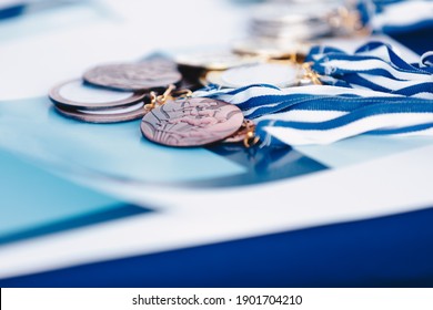 A Bunch Of Marathon Finisher's Medals Lying On Certificate. Race Running Medals From Marathon On Blue Background