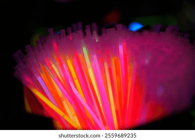 A bunch of neon colored plastic straws are lit up in a dark room. The bright colors and glowing lights create a fun and energetic atmosphere - Powered by Shutterstock