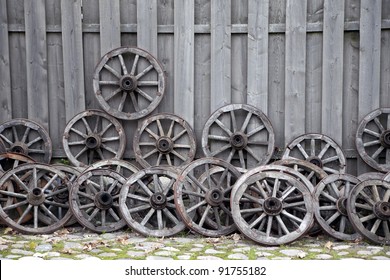 Bunch of old wooden carriage wheels against wooden fence